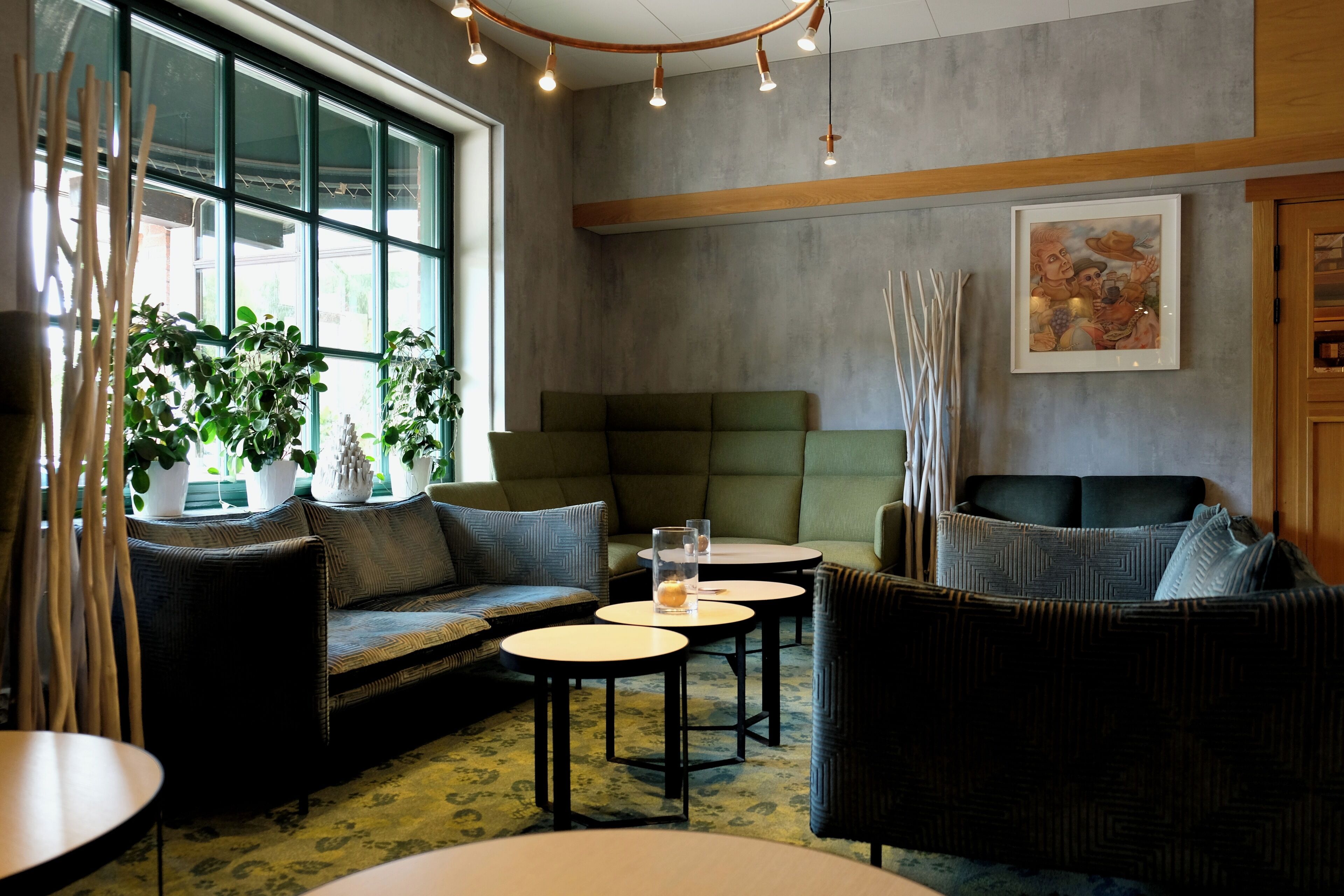 A modern lounge area with a sofa, two round tables, and a green cushioned bench.