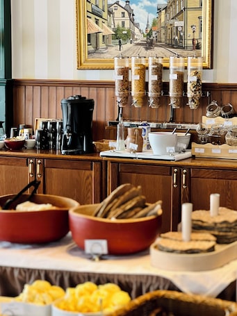 A breakfast buffet with various food items, coffee machines, and a painting of a street scene on the wall.