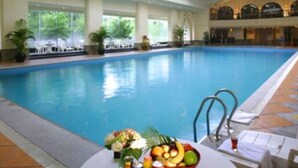 An indoor swimming pool with a high ceiling, a seating area with tables and chairs, and a fruit bowl on the poolside. - Ningbo Nanyuan Hotel (Ningbo)