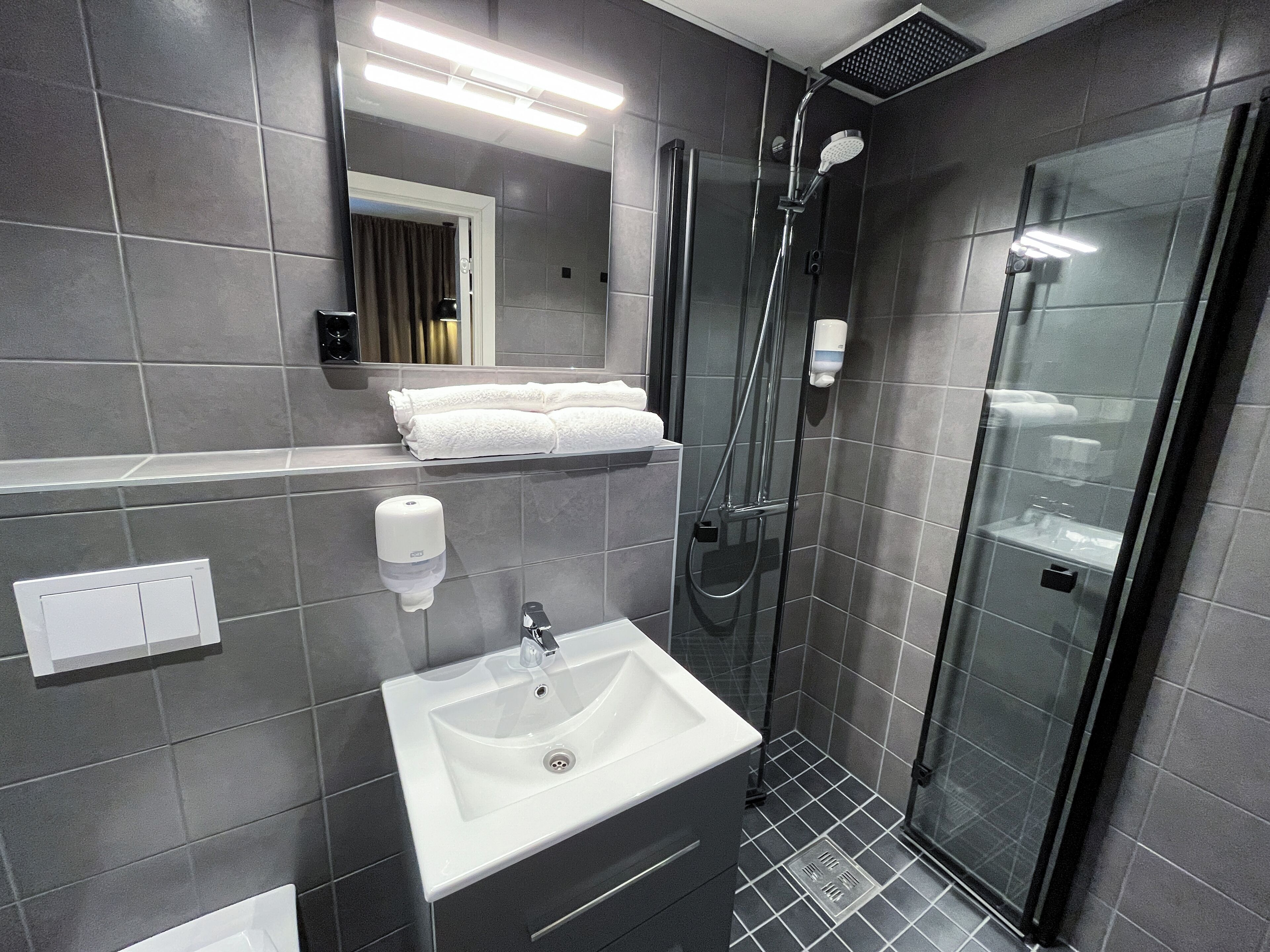 Un baño moderno con ducha de vidrio, un lavamanos blanco y un perchero para toallas.