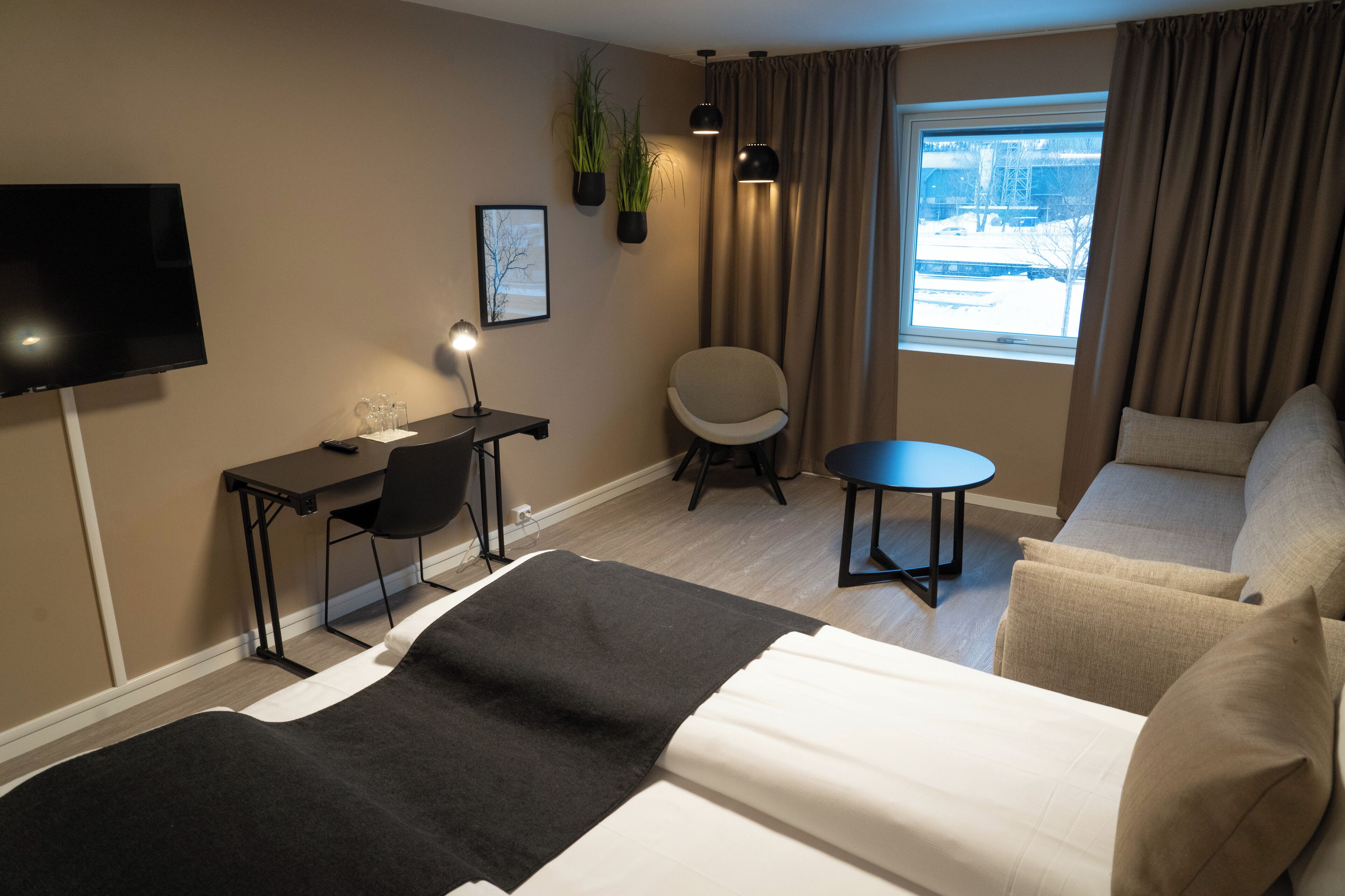 Moderni hotellihuone, jossa on sänky, työpöytä tuolilla, pieni pöytä ja sohva.