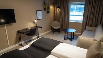 Moderni hotellihuone, jossa on sänky, työpöytä tuolilla, pieni pöytä ja sohva.