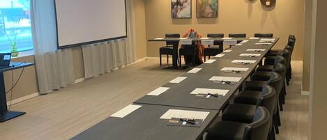 A conference room with a long table, chairs, a projector screen, and a large window.