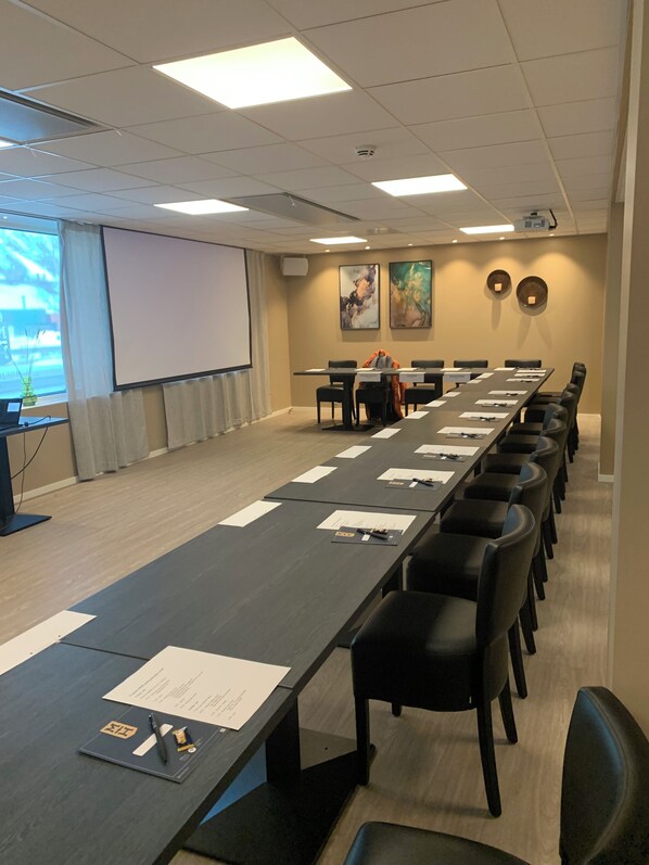 A conference room with a long table, chairs, a projector screen, and a large window.