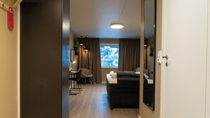 Une chambre d’hôtel avec un lit, un bureau, une chaise, une fenêtre avec des rideaux et une plante.