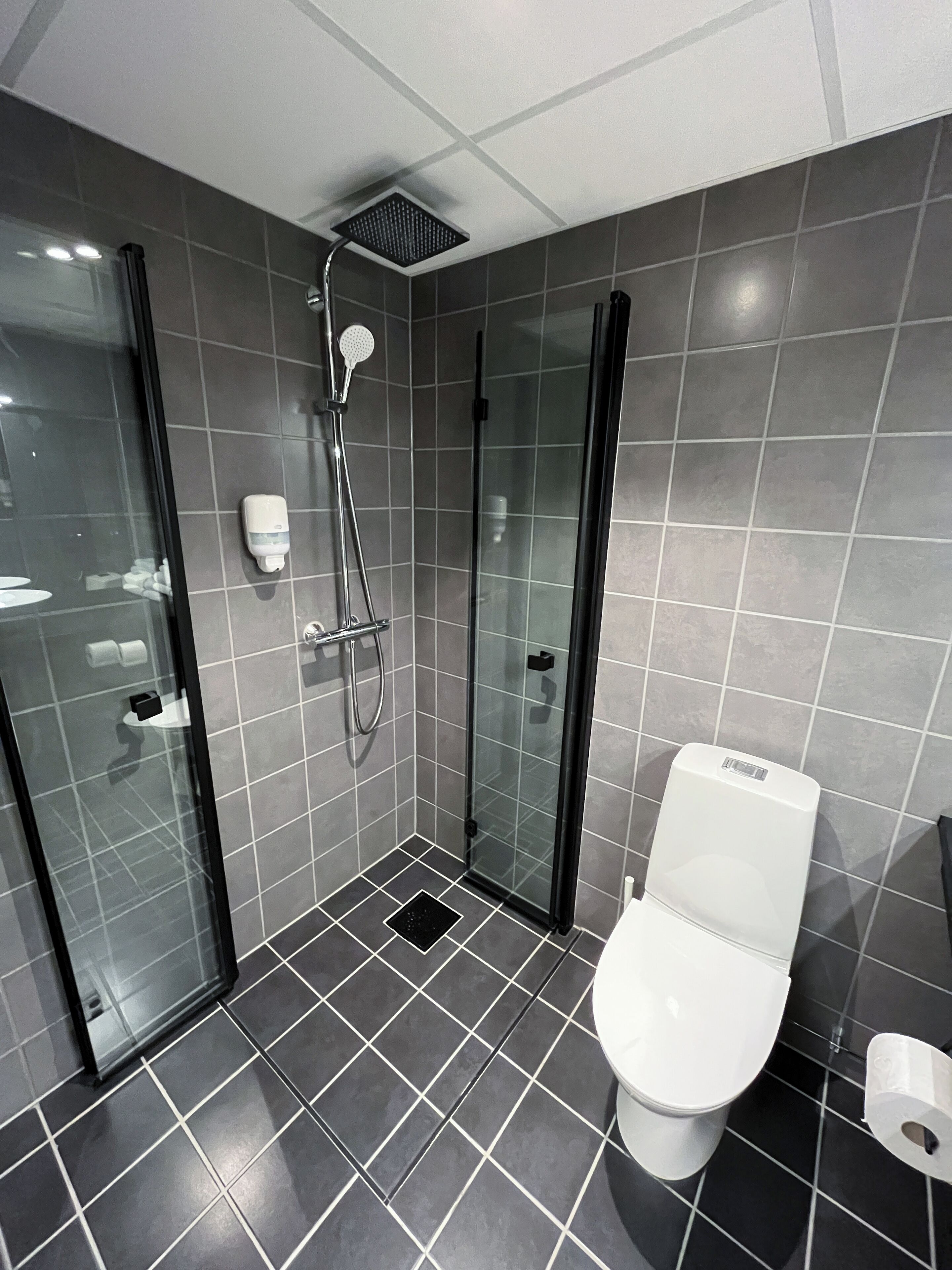 Een moderne badkamer met een douchecabine van glas, een toilet en een zeepdispenser.