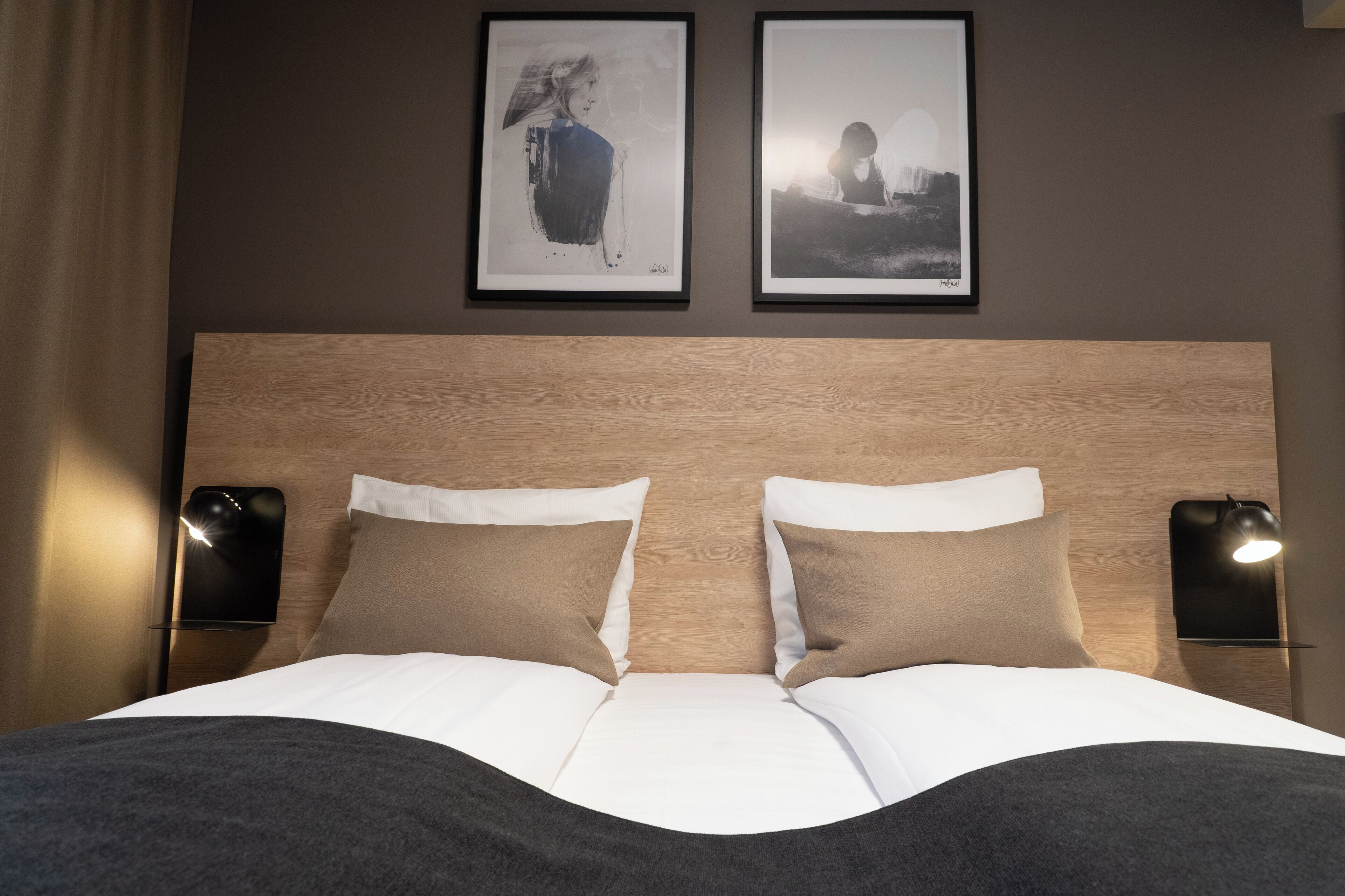 A neatly made bed with two pillows, a wooden headboard, and two wall-mounted lamps.