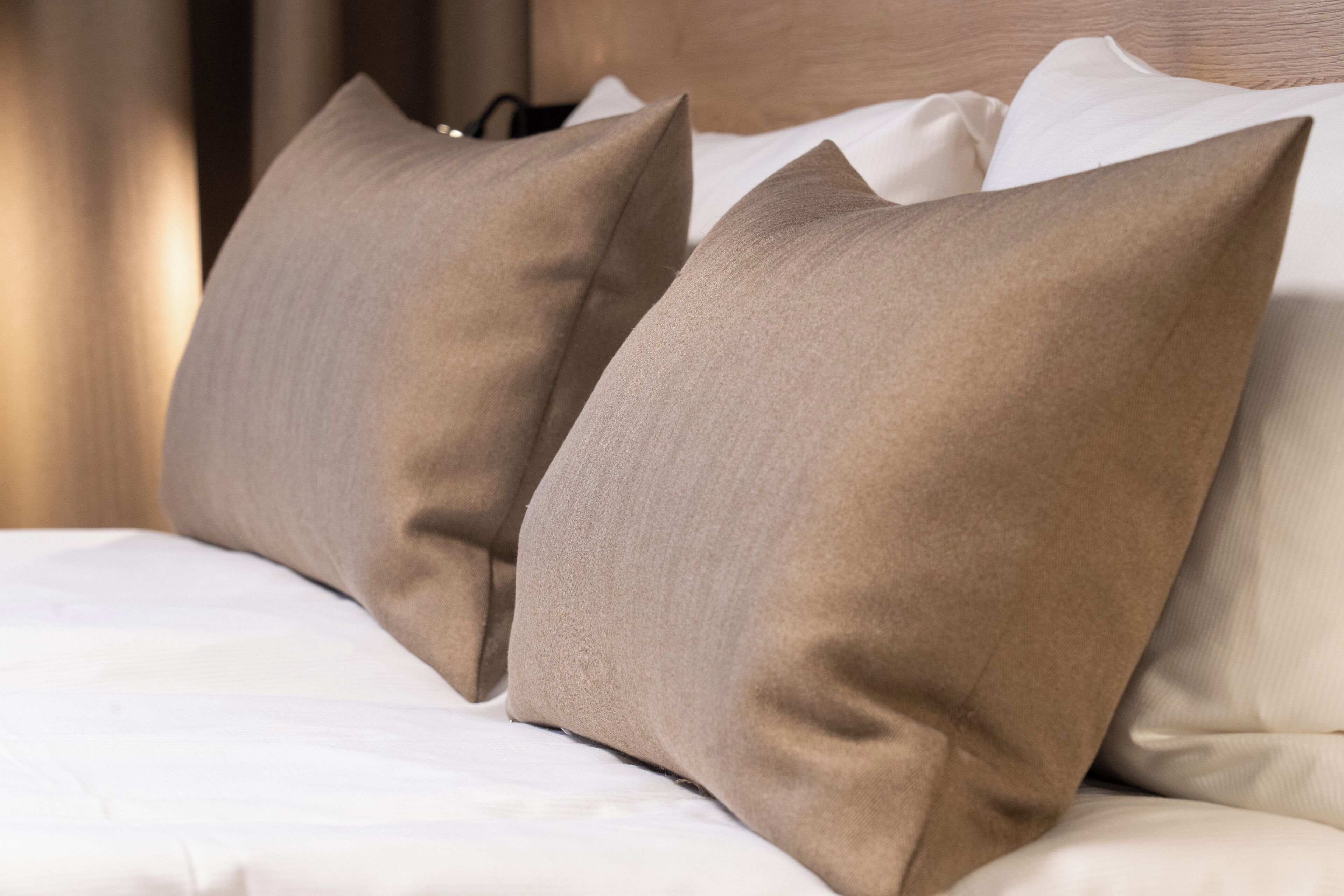 Ein ordentlich bezogenes Bett mit beigen Kissen und weißen Leinen.