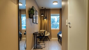 Une chambre d’hôtel moderne avec un plancher en bois, un coin repas comprenant une table et des chaises, un grand miroir et une fenêtre donnant sur des arbres.