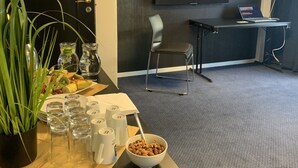 Une salle de conférence dotée d’un grand écran affichant un paysage de montagne, une table sur laquelle se trouvent un bol de noix, des verres et une plante.