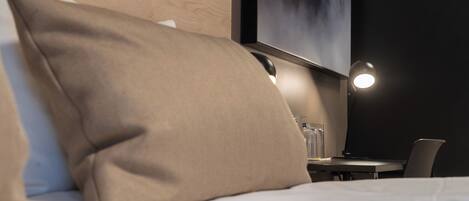 A hotel room with a bed, a desk, and a chair. There is a painting on the wall and a lamp on the desk.