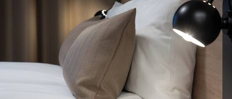 Una cama bien hecha con almohadas y una lámpara de noche negra.