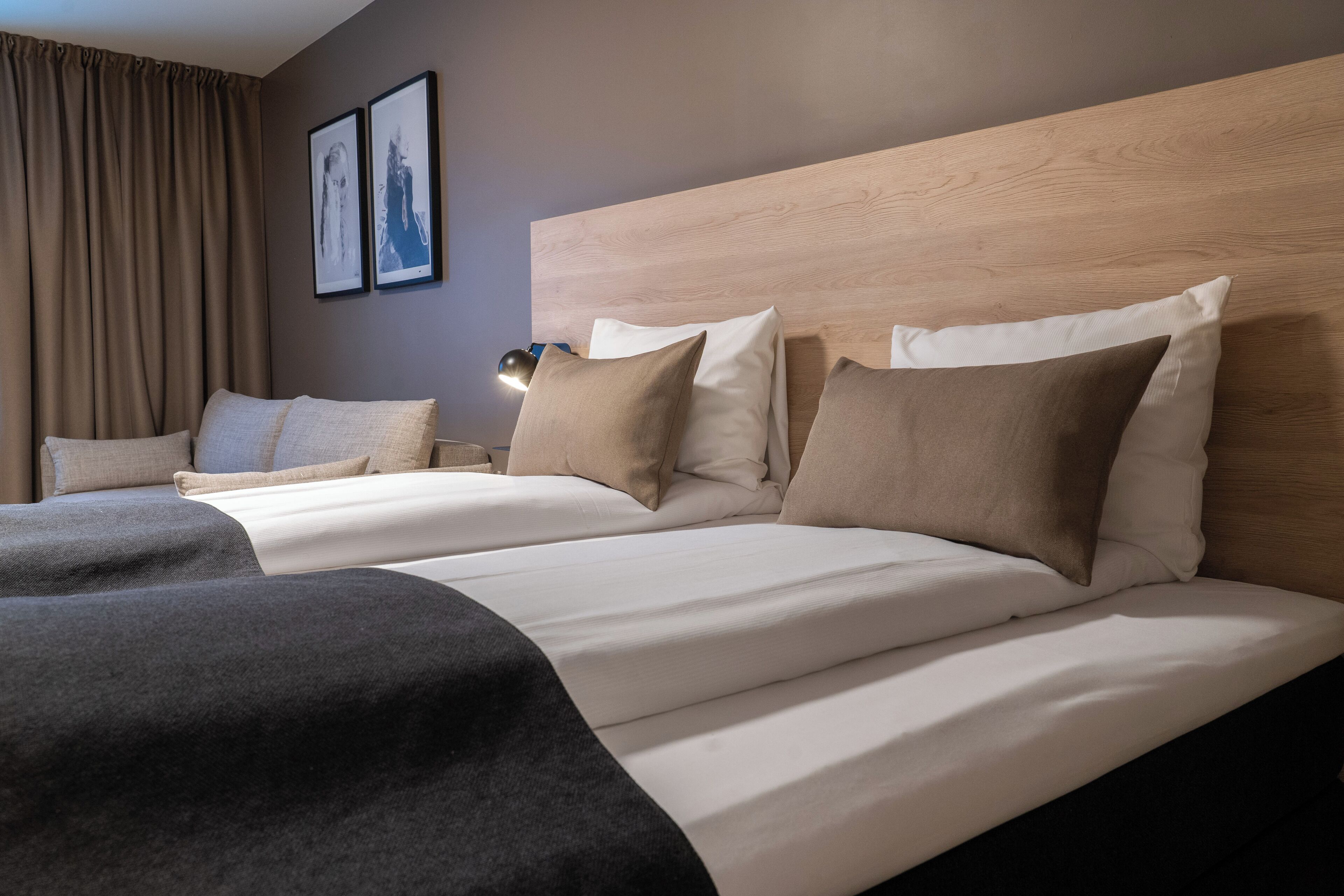 Een hotelkamer met twee bedden, een houten hoofdbord en een groot raam met gordijnen.