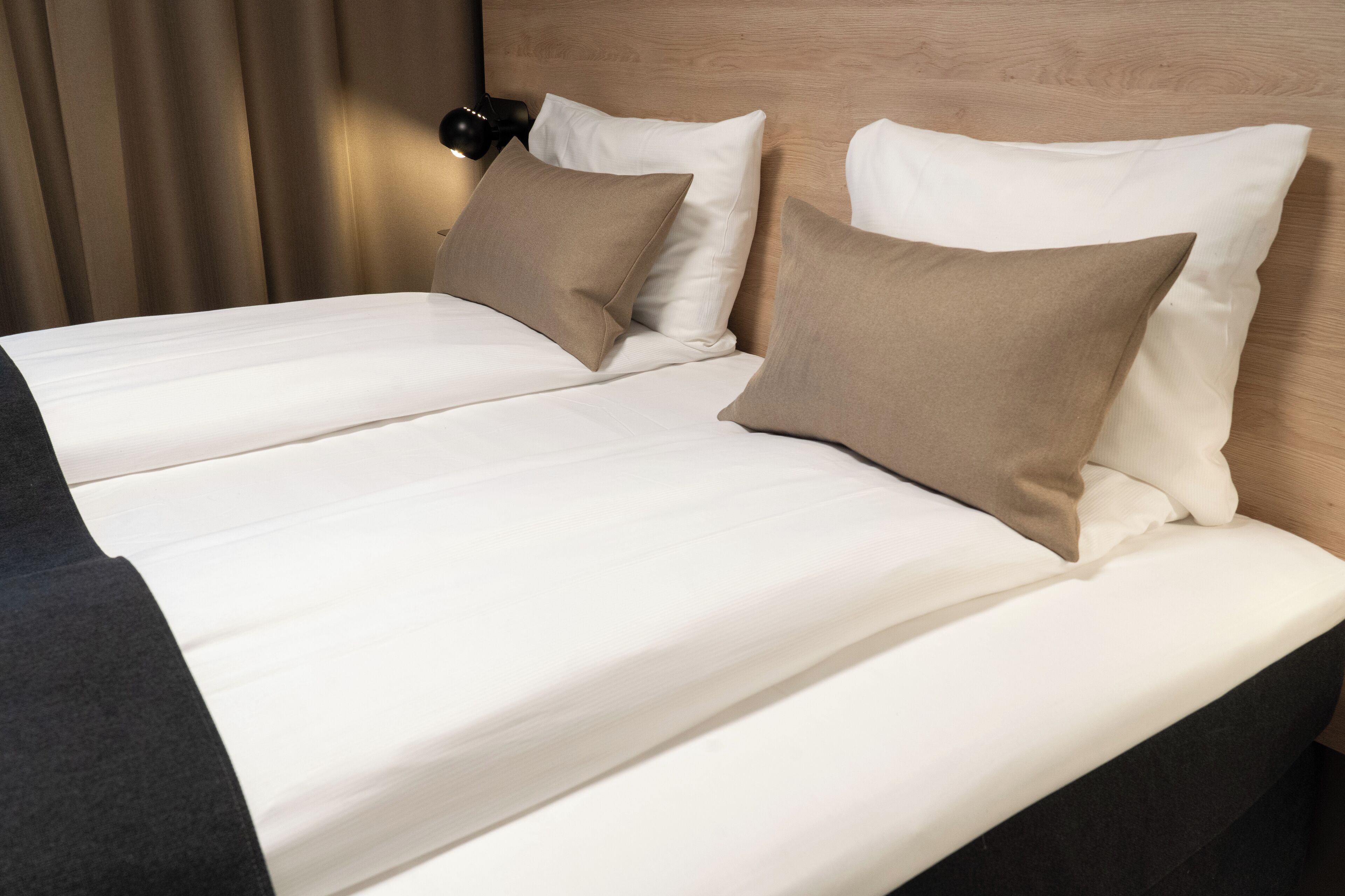 Un lit double avec une literie blanche et beige, une tête de lit en bois et une lampe de chevet noire.