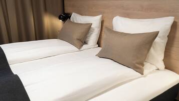 Una cama doble con ropa de cama blanca y color crema, un cabecero de madera y una lámpara de noche negra.