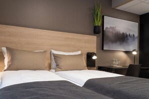 A neatly made bed with two pillows, a bedside table with a lamp, a framed picture on the wall, and a potted plant. - Mosjoen Hotell  (Mosjoen)