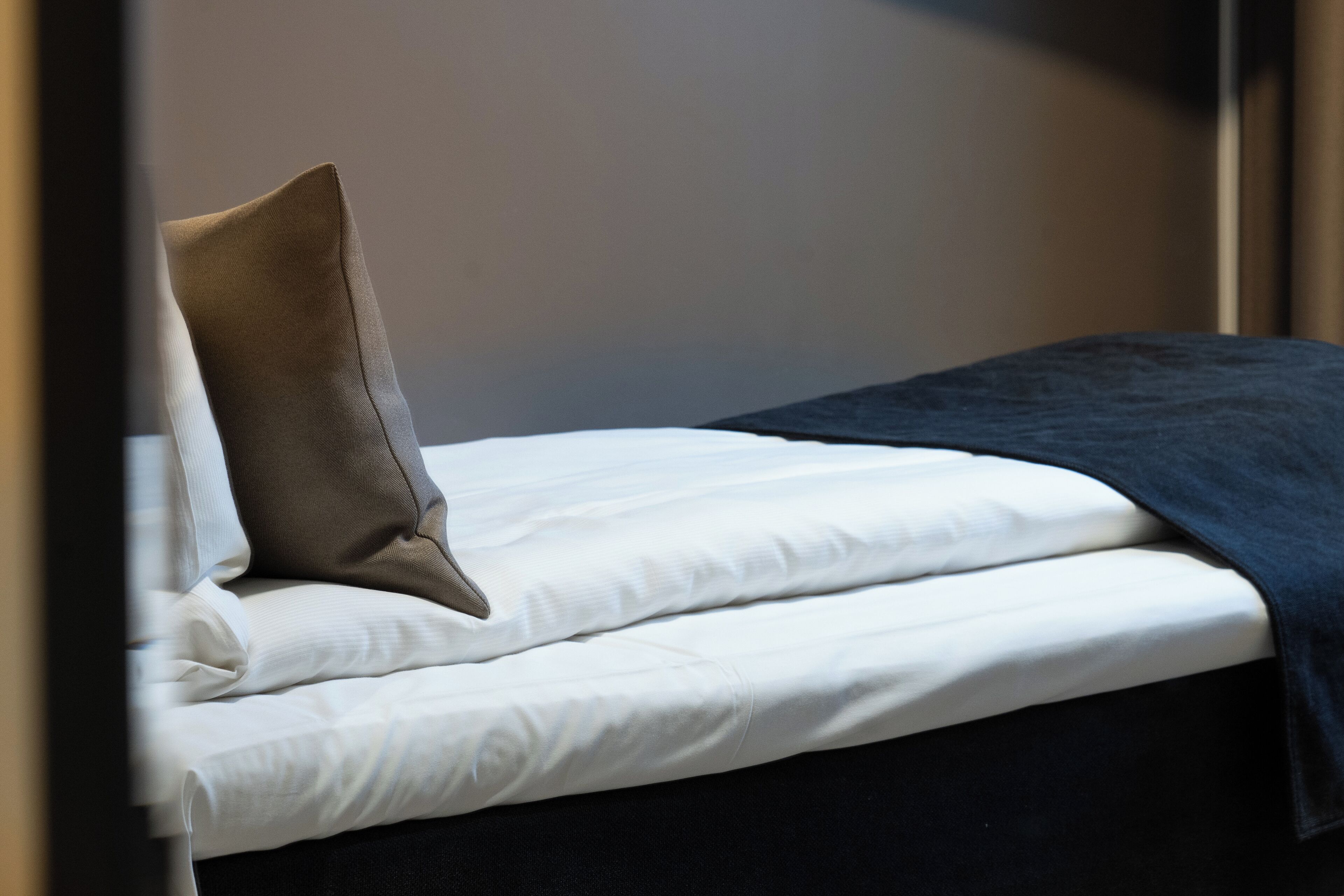 A neatly made bed with white linens and a dark blue blanket.