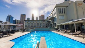 Una piscina en la azotea con sillas de descanso y el horizonte de la ciudad al fondo.