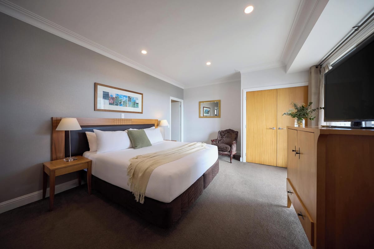 A hotel room with a bed, a nightstand, a lamp, a chair, a wardrobe, and a television.