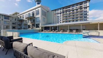 A swimming pool with lounge chairs and a covered seating area, surrounded by modern buildings with balconies.