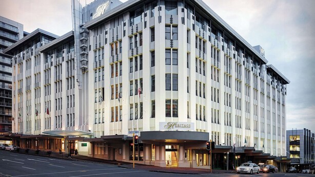 Un hotel grande y moderno con un cartel llamativo que dice 'Heritage', varias banderas y una ubicación en una esquina, en una intersección.