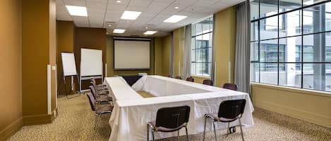 Una sala de conferencias con una larga mesa, sillas, una pizarra y una pantalla de proyector.