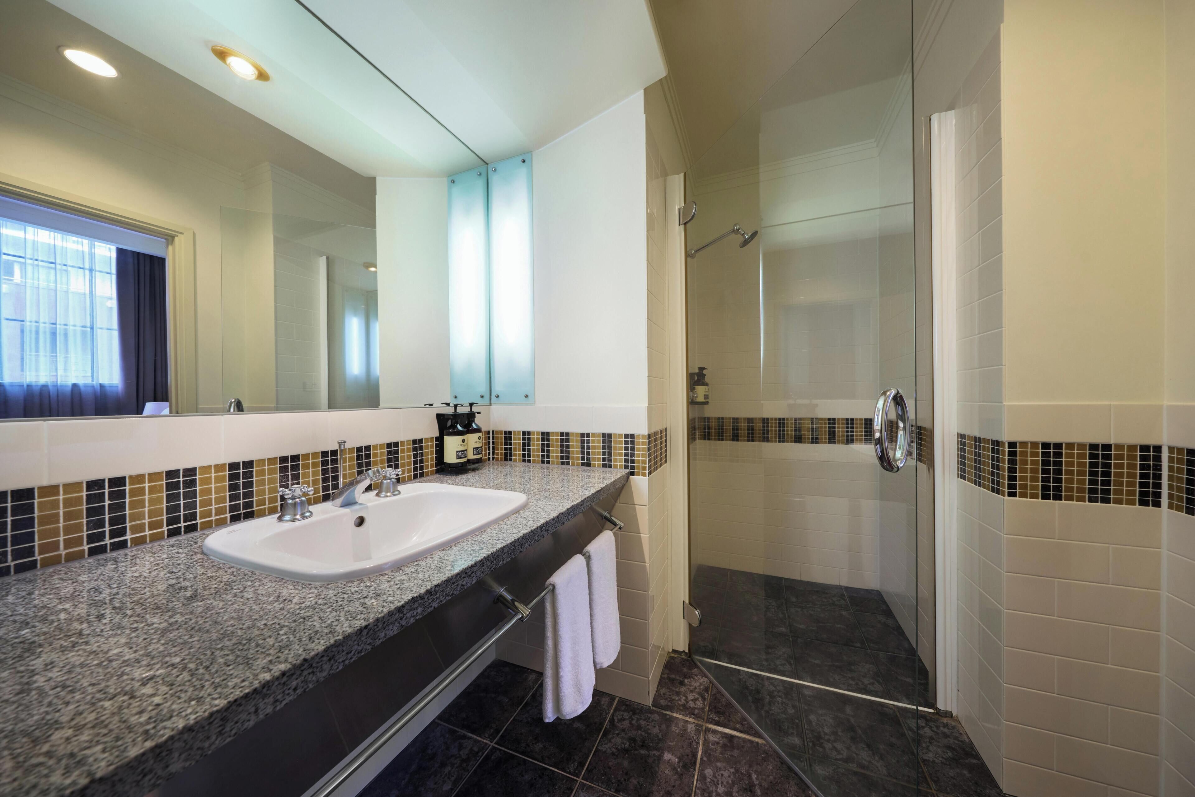 A bathroom with a double sink, a glass shower enclosure, and a large mirror.