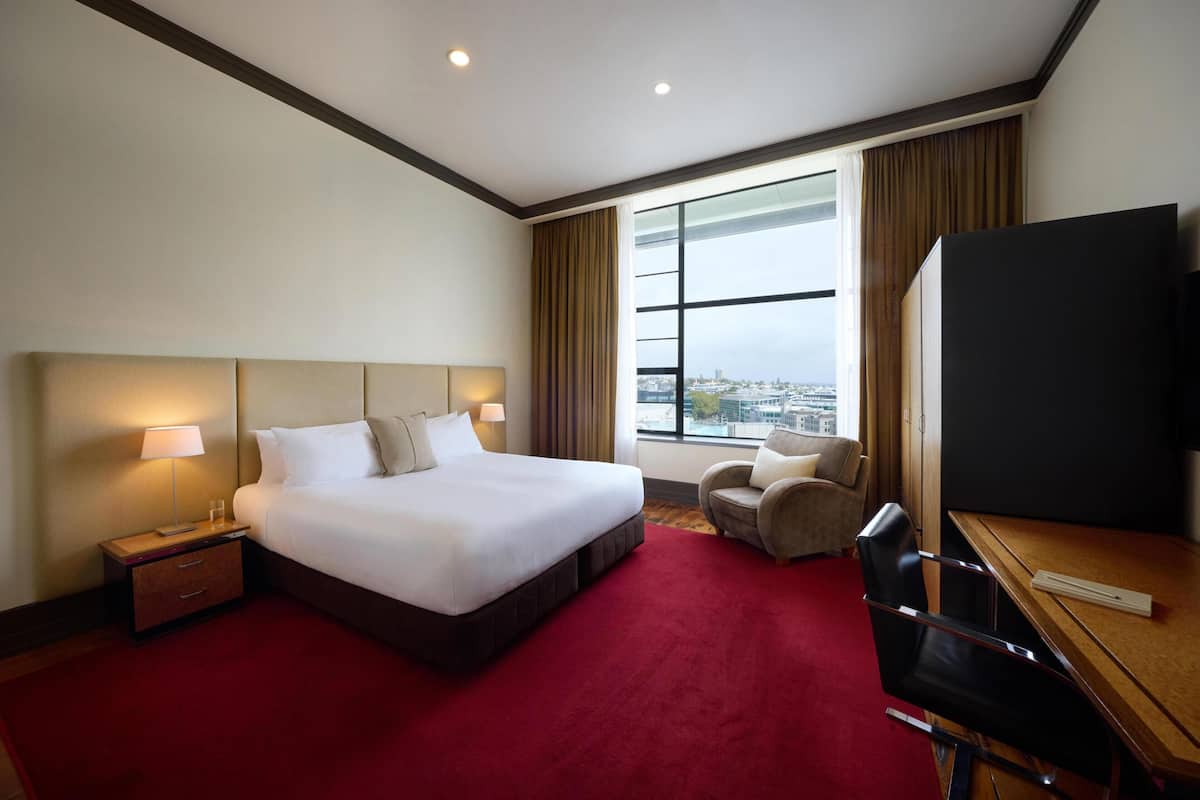Une chambre d’hôtel avec un grand lit, un bureau, une chaise, une télévision et une fenêtre donnant sur la ville.