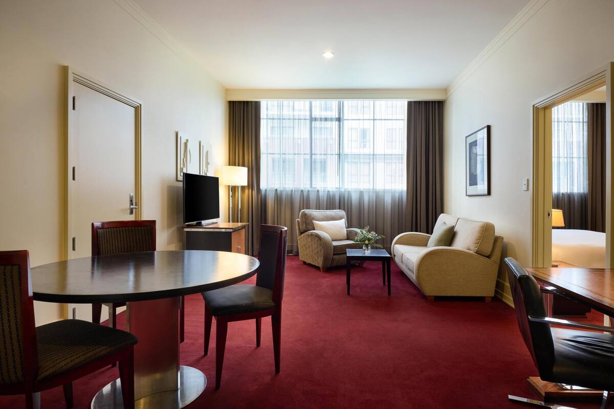 Une chambre d’hôtel équipée d’une table à manger, de deux canapés, d’un téléviseur et d’une grande fenêtre avec des rideaux.