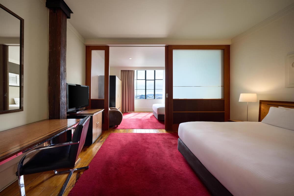 Une chambre d’hôtel avec un lit, un bureau et une chaise, une télévision et une fenêtre avec des rideaux.
