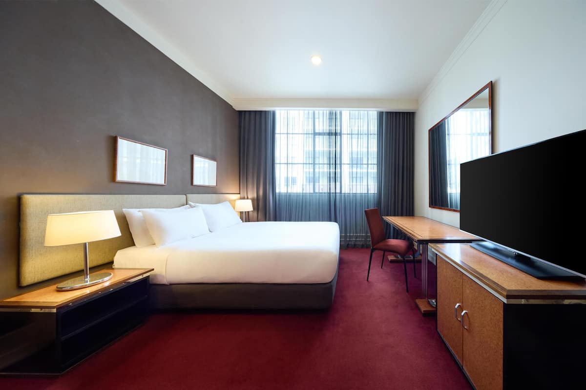 Une chambre d’hôtel avec un lit, un bureau, une télévision et une fenêtre avec des rideaux.