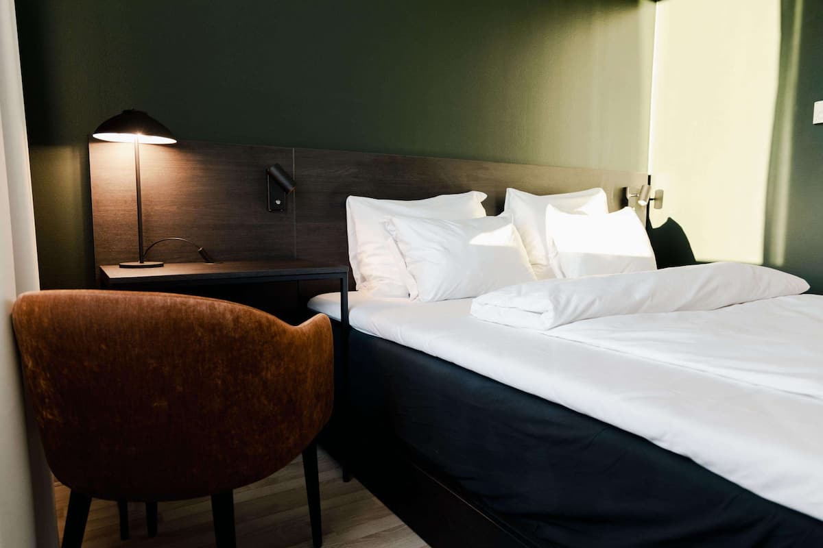 Een hotelkamer met een bed, nachtkastje, lamp en stoel.