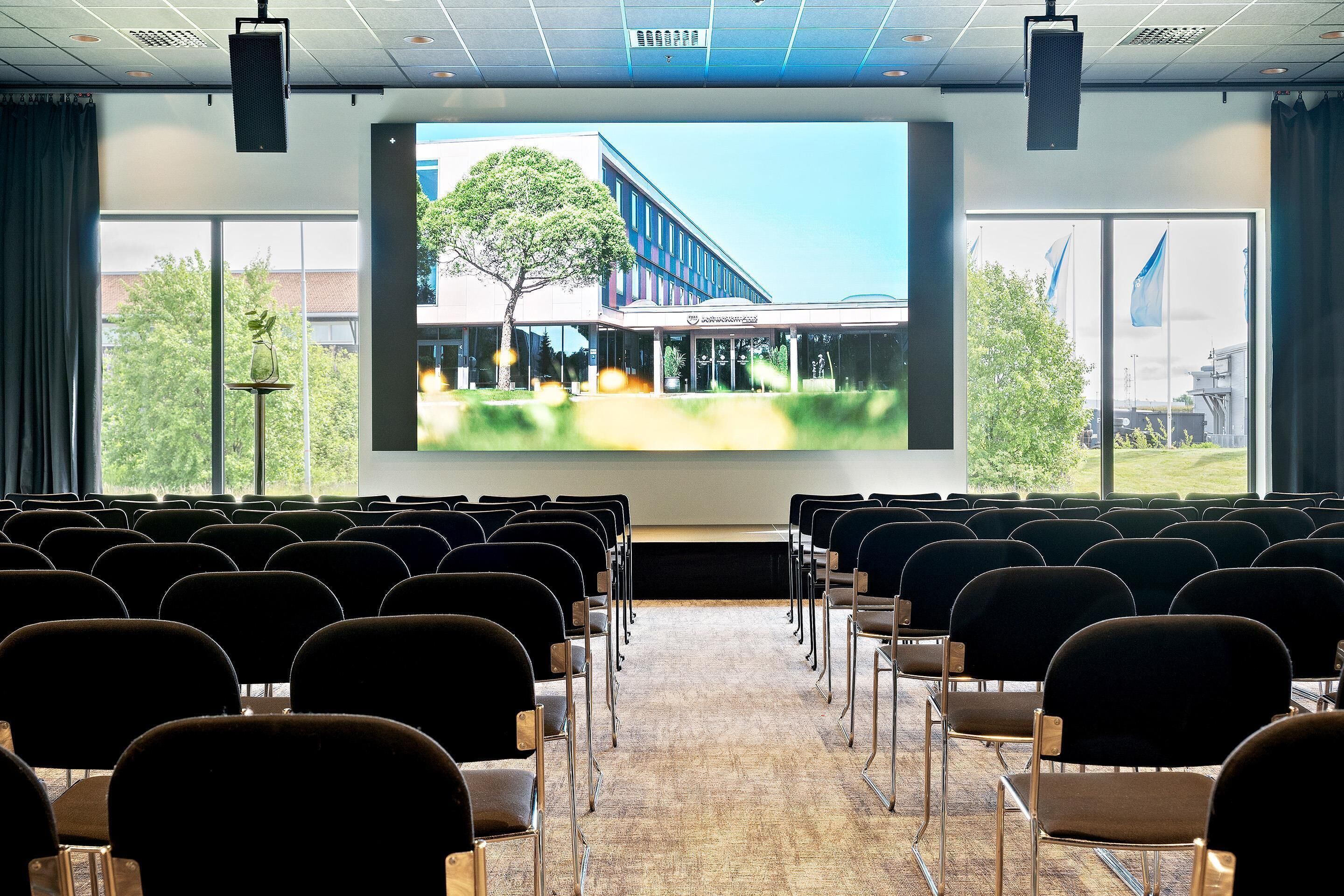 A conference room with rows of chairs facing a large screen displaying a building exterior.