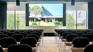 A conference room with rows of chairs facing a large screen displaying a building exterior.