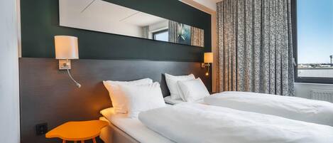 Habitación de hotel con dos camas, un taburete naranja pequeño, una lámpara de pared y un ventanal con cortinas.