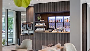 Een moderne bar met een wand van houten panelen, drankflessen op planken, en een zithoek met banken en stoelen.