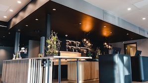 Een modern receptiegebied met een houten receptiebalie, een zwarte toonbank en een bar met planken en verlichting.