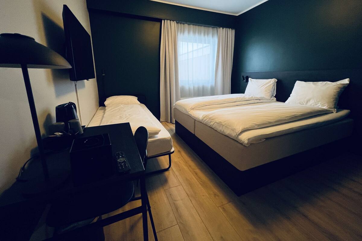 Een hotelkamer met een bed, een bureau met stoel, een televisie en een raam met gordijnen.