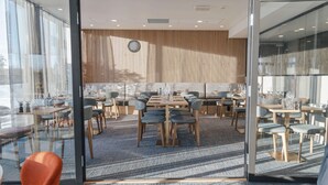 Een modern restaurant met glazen wanden, houten paneelwanden en diverse zithoeken, waaronder tafels en ruimtes met banken.