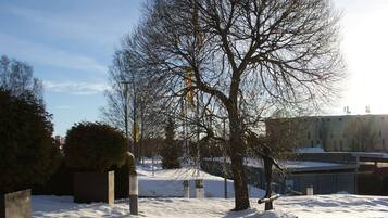 Een besneeud gebied buiten met een grote kale boom, betonnen paaltjes en een gebouw op de achtergrond.