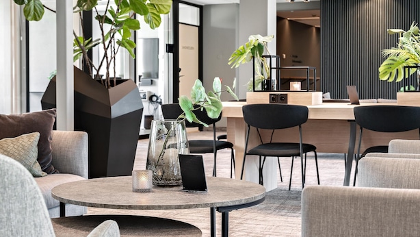 Een moderne zithoek met een ronde tafel, comfortabele stoelen en potplanten.