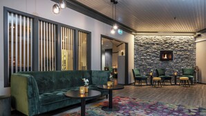 A modern lounge area with a green sofa, round tables, and a stone wall with a fireplace. - Thon Hotel Baronen (Ålesund)