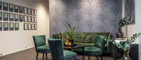 A room with a green sofa, two chairs, a table with a plant, and framed certificates on the wall.