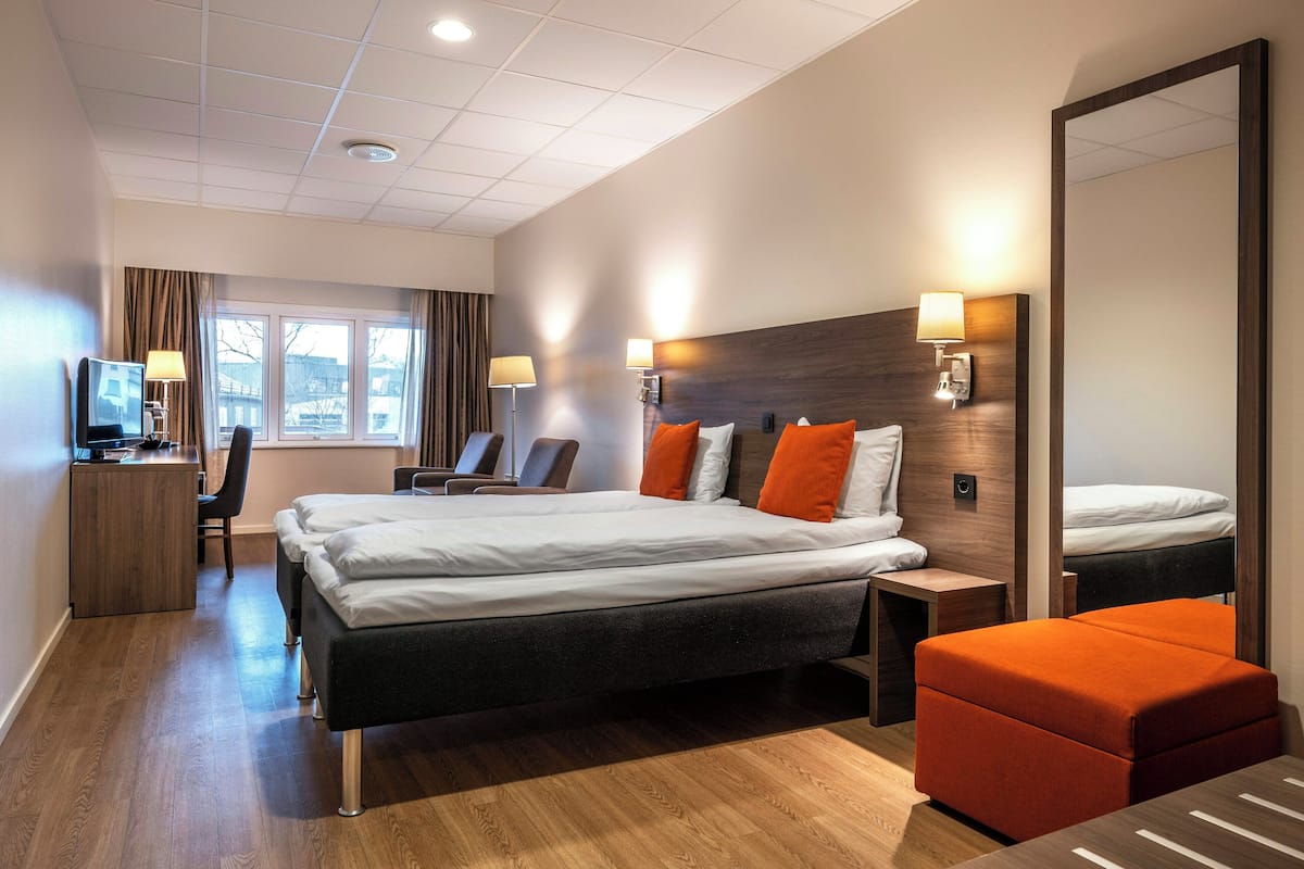 A hotel room with a bed, a desk, a chair, a TV, and a large mirror.