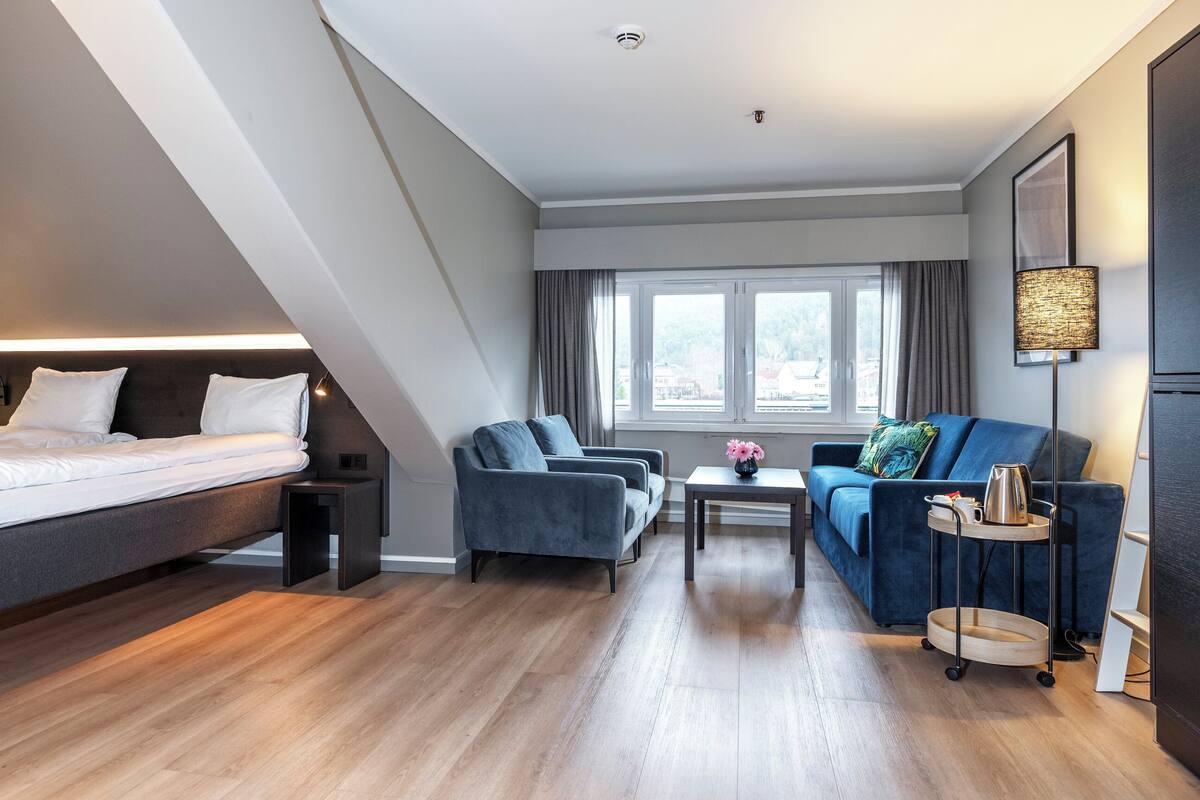 A modern hotel room with a loft bed, a sofa, a coffee table, and a desk.