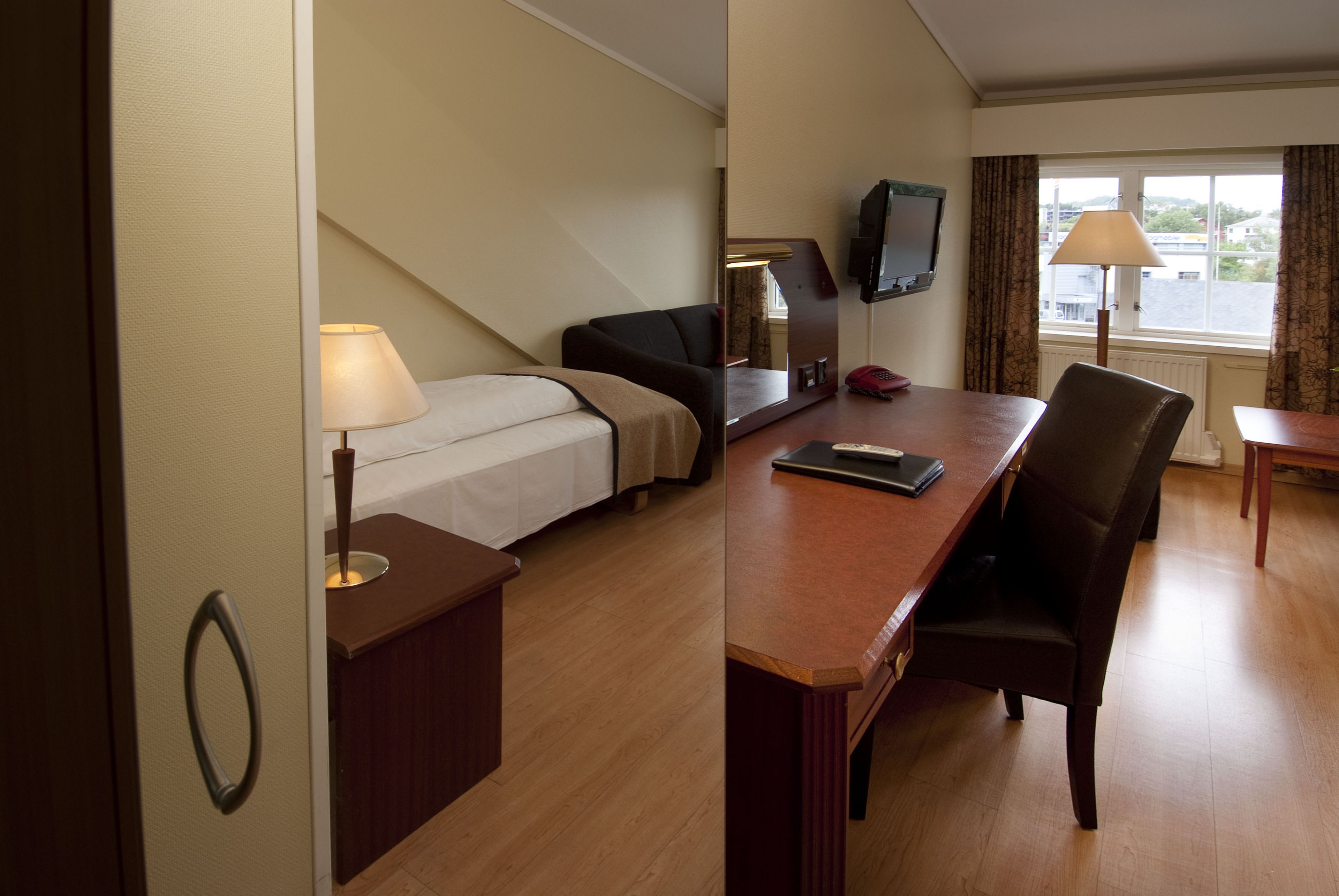 A hotel room with a bed, a desk, a chair, a TV, and a window with curtains.