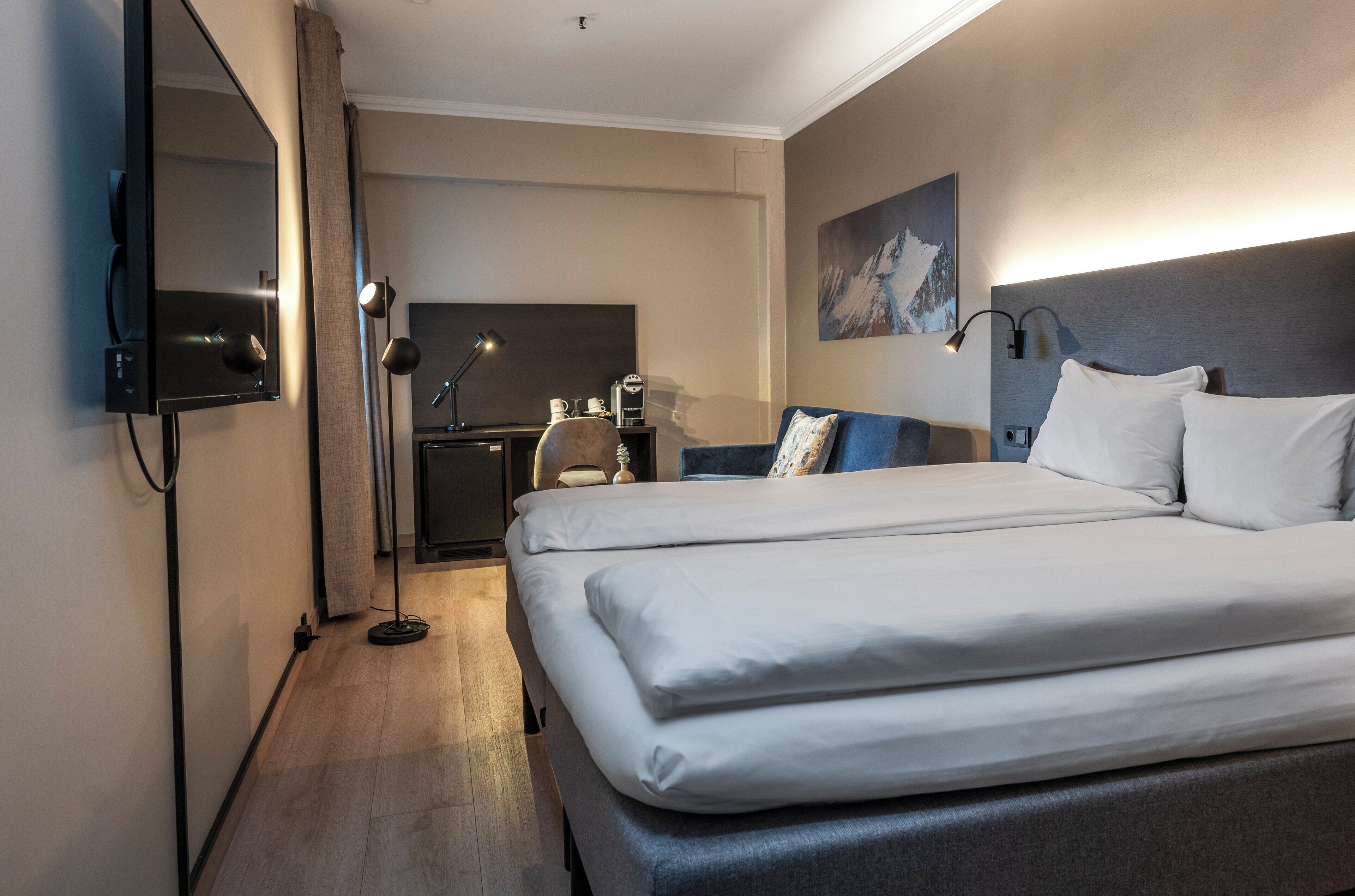 A hotel room with a large bed, a desk, a chair, a flat-screen TV, and a painting on the wall.