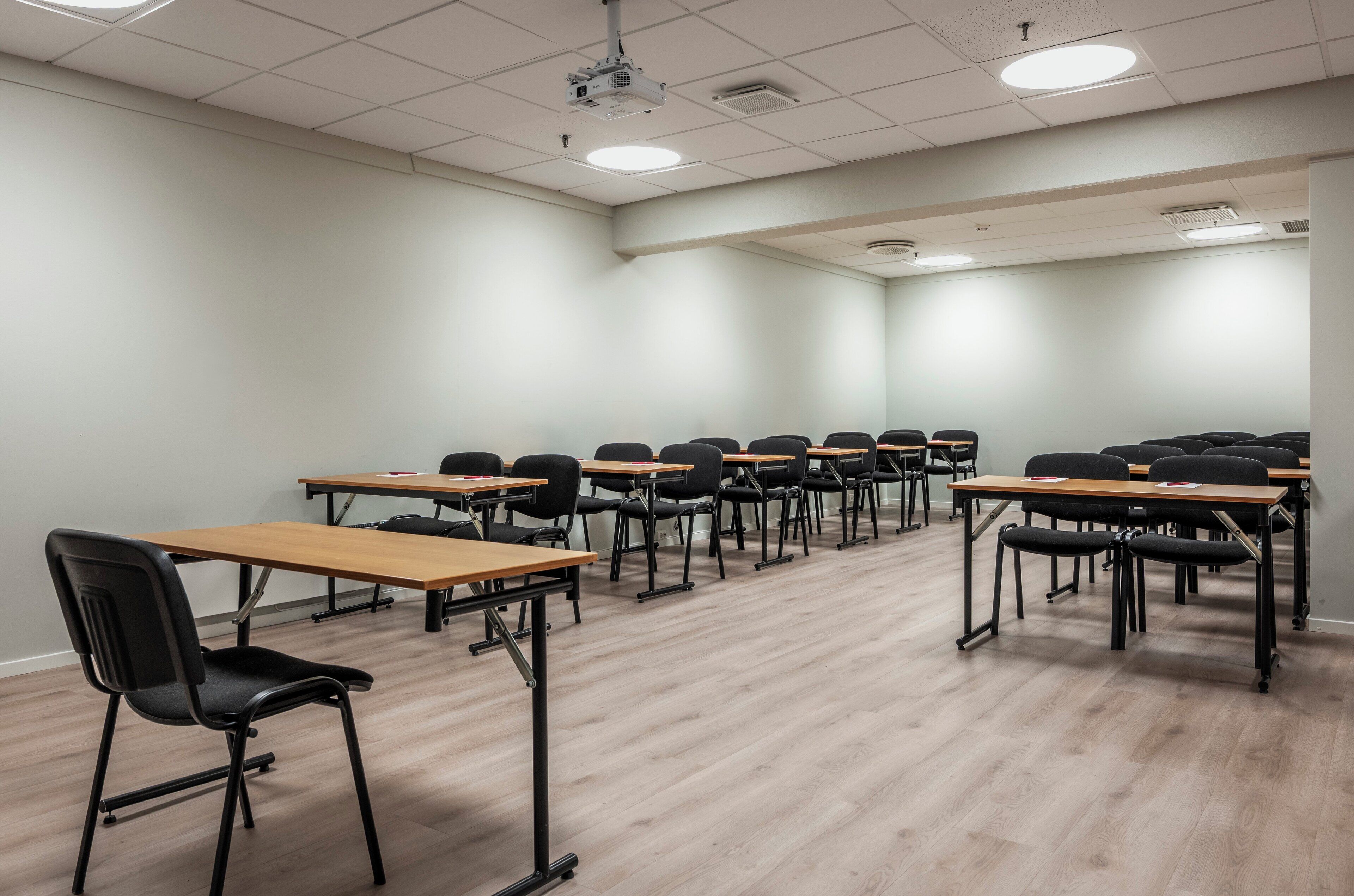 A conference room with rows of tables and chairs, equipped with a projector and ceiling lights.
