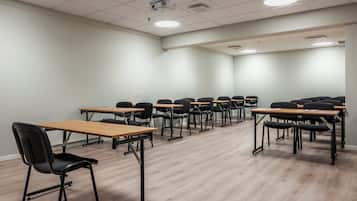 A conference room with rows of tables and chairs, equipped with a projector and ceiling lights.
