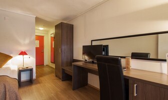 Una habitación de hotel con un escritorio de madera, una silla, un televisor, una lámpara y una cama.